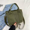 A close-up of a olive green canvas crossbody bag with an adjustable strap resting on a light fabric background.