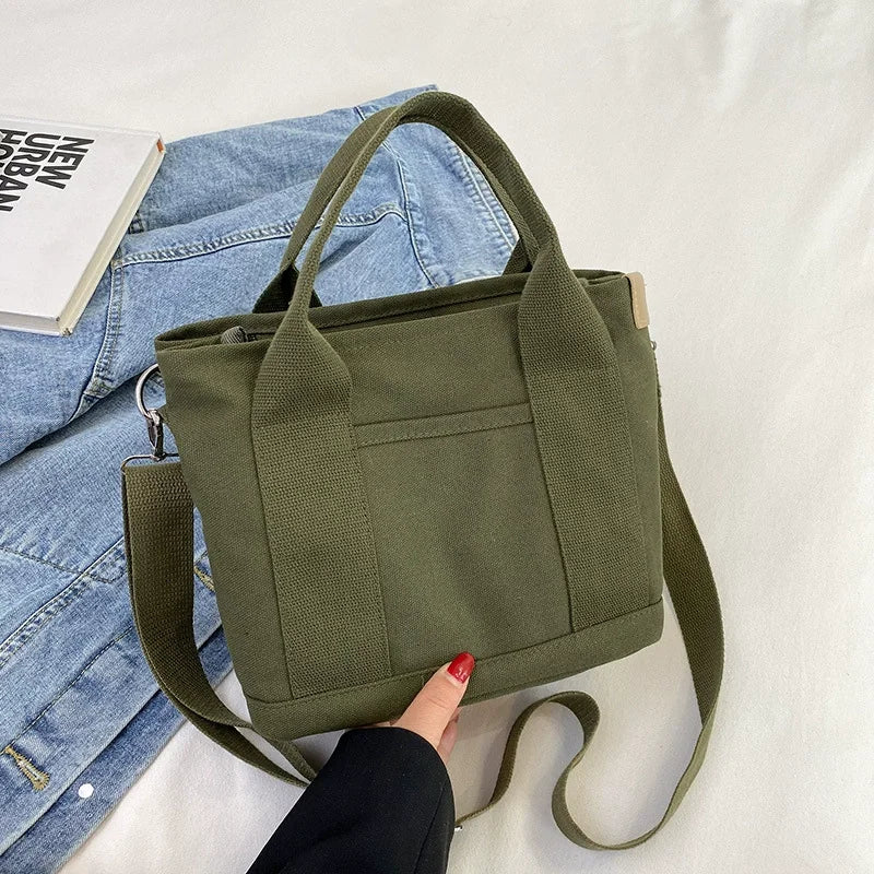 A close-up of a olive green canvas crossbody bag with an adjustable strap resting on a light fabric background.