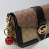 A brown patterned leather handbag with a black strap and a gold fruit charm keychain.
