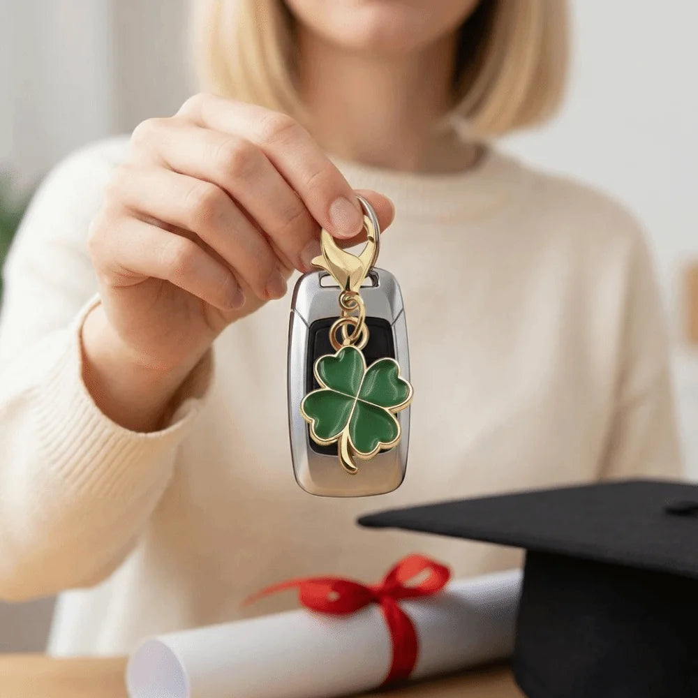 A hand holds a gold and green four leaf clover keychain against a blurred background.