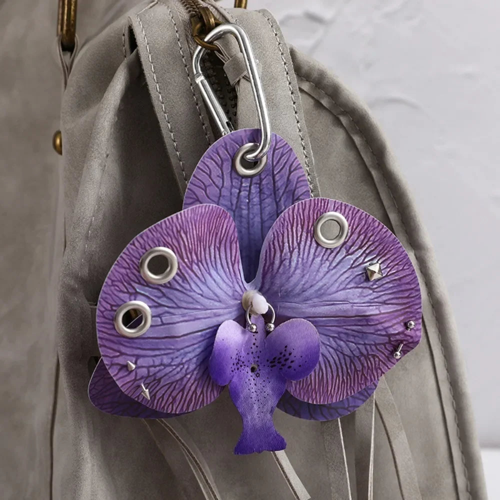 A purple orchid flower keychain hanging from a gray fabric strap.