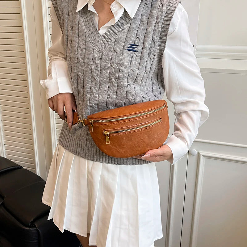 A woman wearing a gray knitted vest and white shirt holds an orange leather crossbody bag.