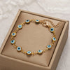 Gold charm bracelet featuring blue evil eye beads on an adjustable chain, displayed in a box.