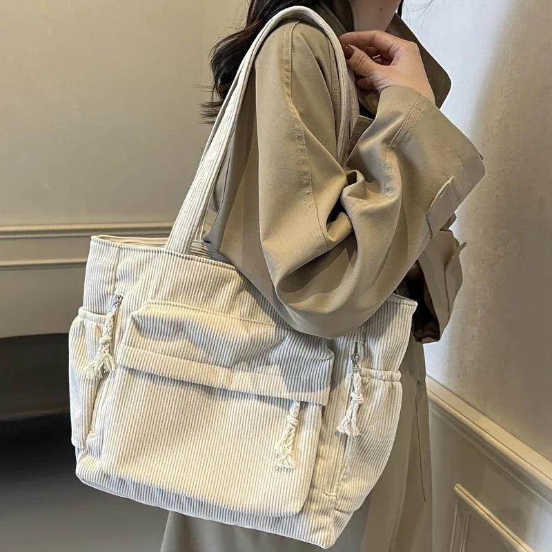A light beige corduroy shoulder bag with a zipper is being held by a person.