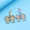 Silver and gold leopard print bow and heart bag charm keychain on a light blue background