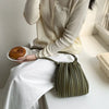 A woman wearing a cream-colored top and white pants holds a olive green PU leather pleated crossbody bag.