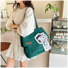 A woman holds a dark green canvas tote bag featuring a white Snoopy design in a light beige outfit.
