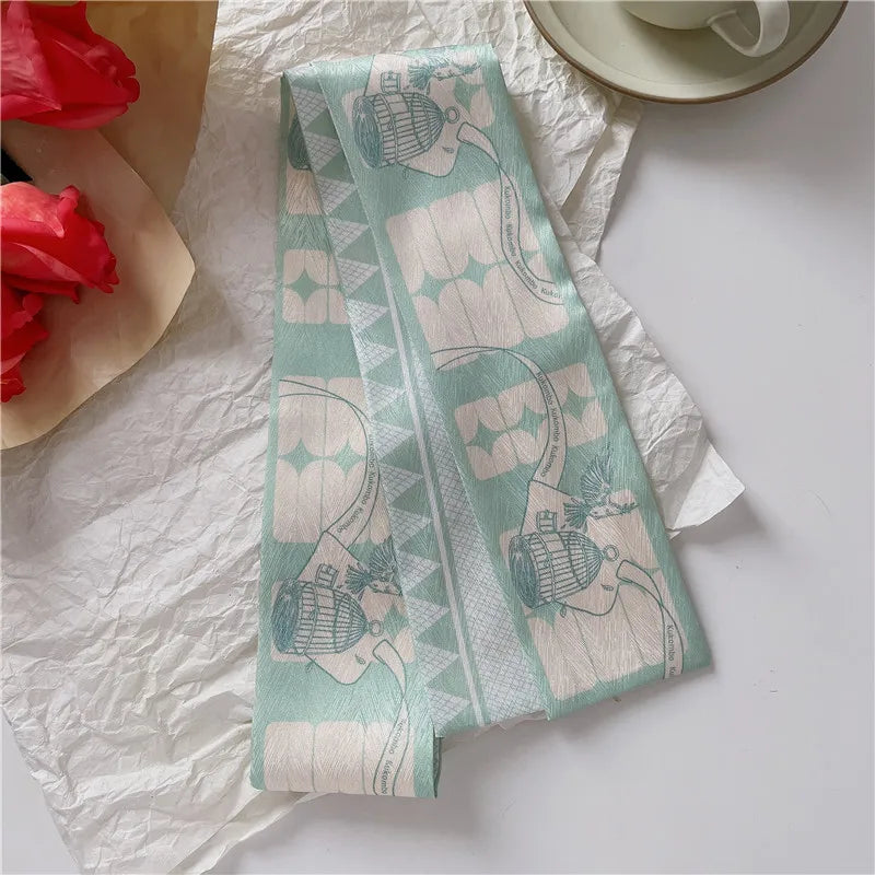 Un foulard de cheveux en soie vert menthe clair avec un motif délicat est posé sur du papier blanc.
