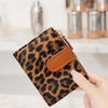 A hand holds a brown leopard print PU leather bifold wallet with a zipper closure.
