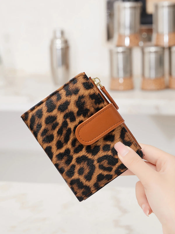 A hand holds a brown leopard print PU leather bifold wallet with a zipper closure.