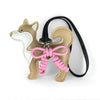 Charm de perro Shiba Inu hecho de cuero beige y blanco con un lazo rosa trenzado a mano en una correa negra.