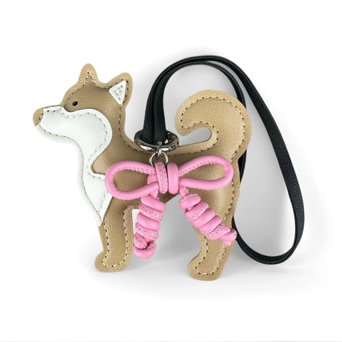 Charm de perro Shiba Inu hecho de cuero beige y blanco con un lazo rosa trenzado a mano en una correa negra.