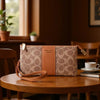 A tan faux leather mini crossbody bag with a monogram pattern rests on a wooden table in a warm interior setting.