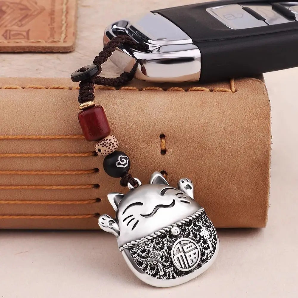 A silver lucky cat keychain with facial markings and a patterned cover is displayed on a brown leather card.