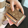 Une main tient un porte-cartes en cuir PU marron contenant diverses cartes et pièces sur une surface sombre.