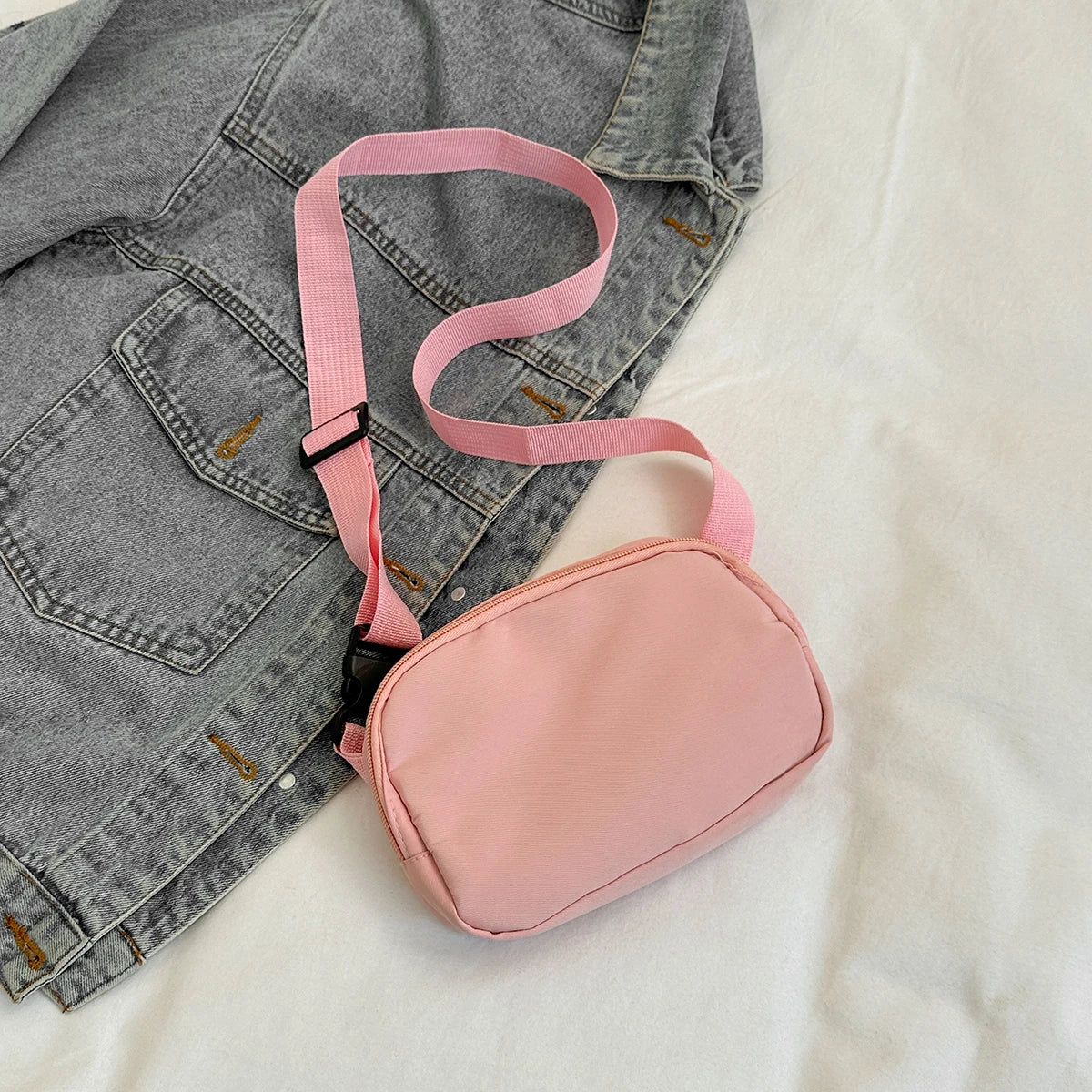 A pink nylon cross-body waist bag with a strap is shown against a white background.