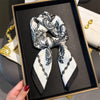 A black framed photo displays an elegant paisley silk hair scarf tied in a bow.