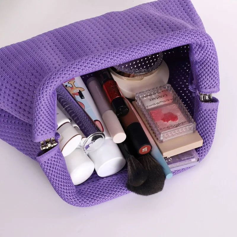 A purple knitted clip bag is open, displaying various makeup and beauty tools inside.