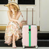 A woman in a floral dress sits next to a pink suitcase with green straps.