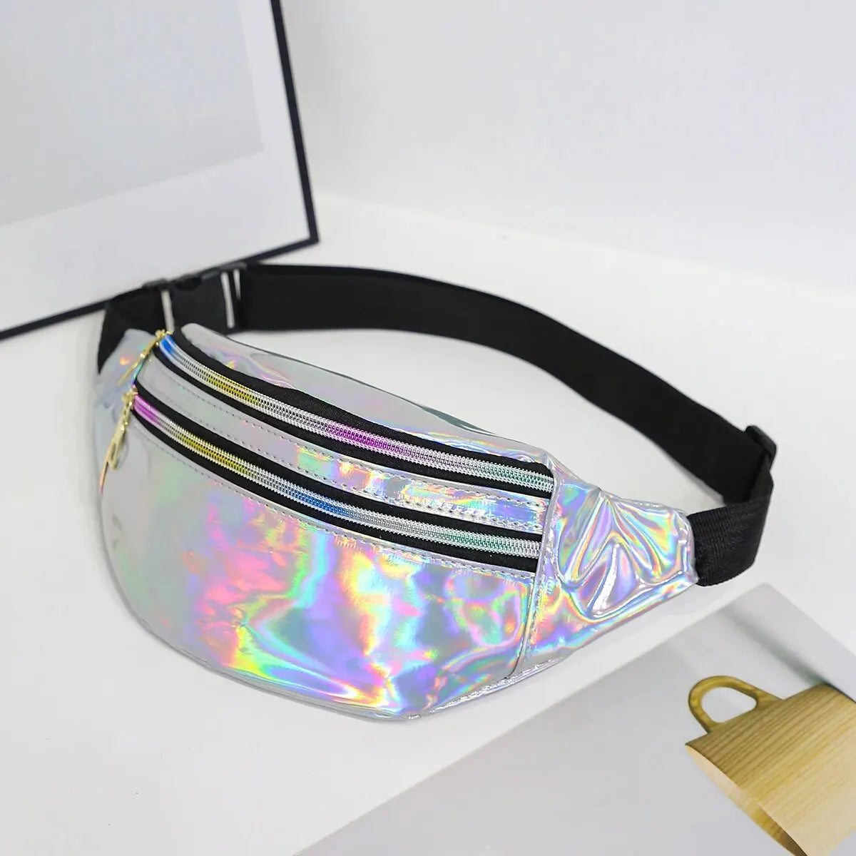 A silver holographic sequin waist bag with a black adjustable strap is displayed on a white surface.