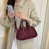 A woman holds a maroon retro crocodile textured mini crossbody bag against a light beige jacket.