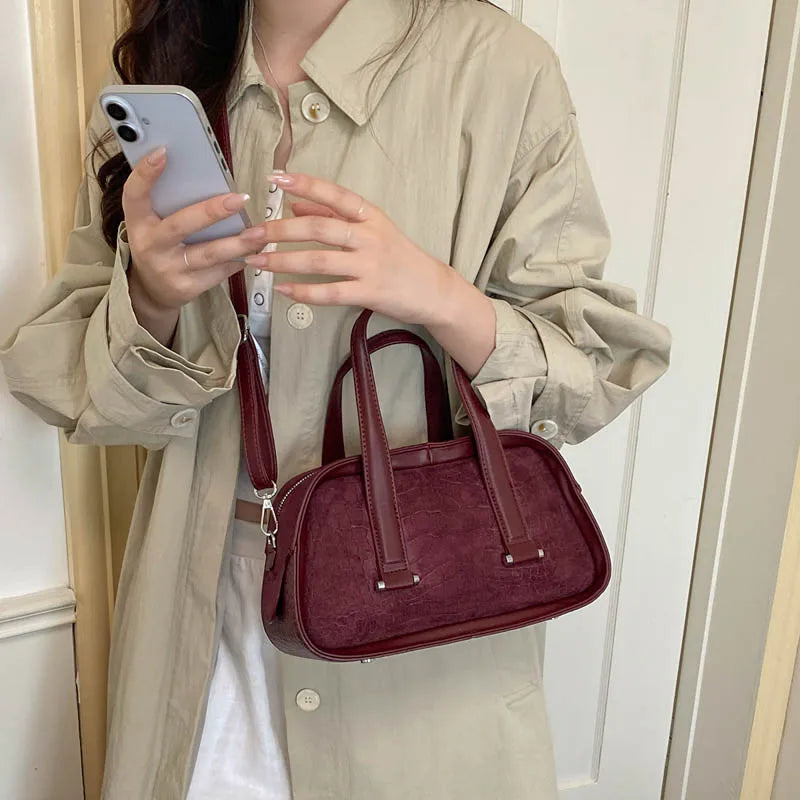 A woman holds a maroon retro crocodile textured mini crossbody bag against a light beige jacket.