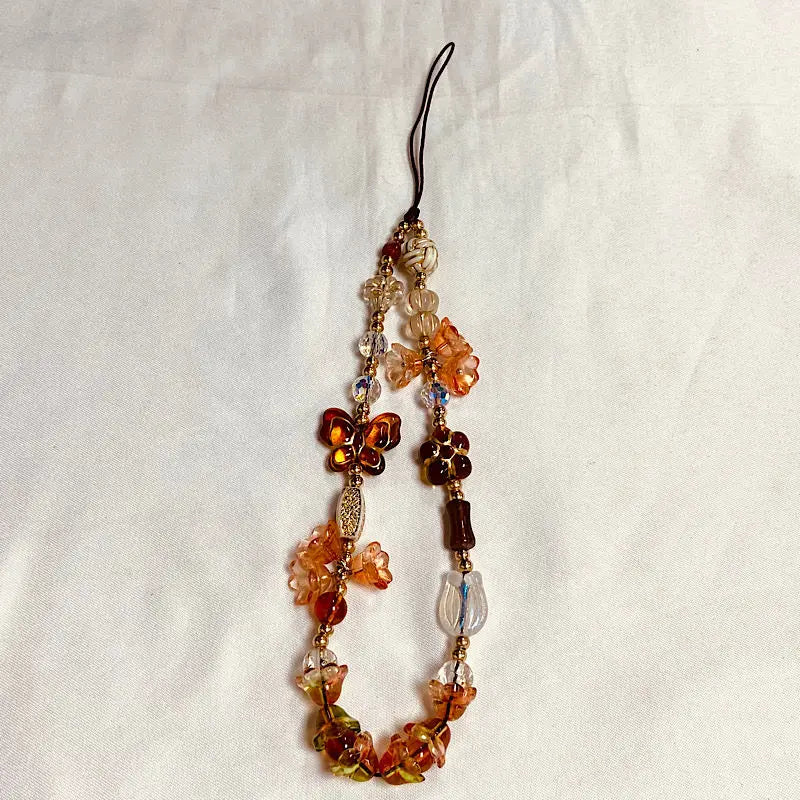 A beaded phone charm strap with an anti-lost lanyard featuring amber and gold colored beads.