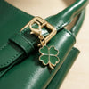 A gold-toned four leaf clover keychain attached to a dark green leather strap.