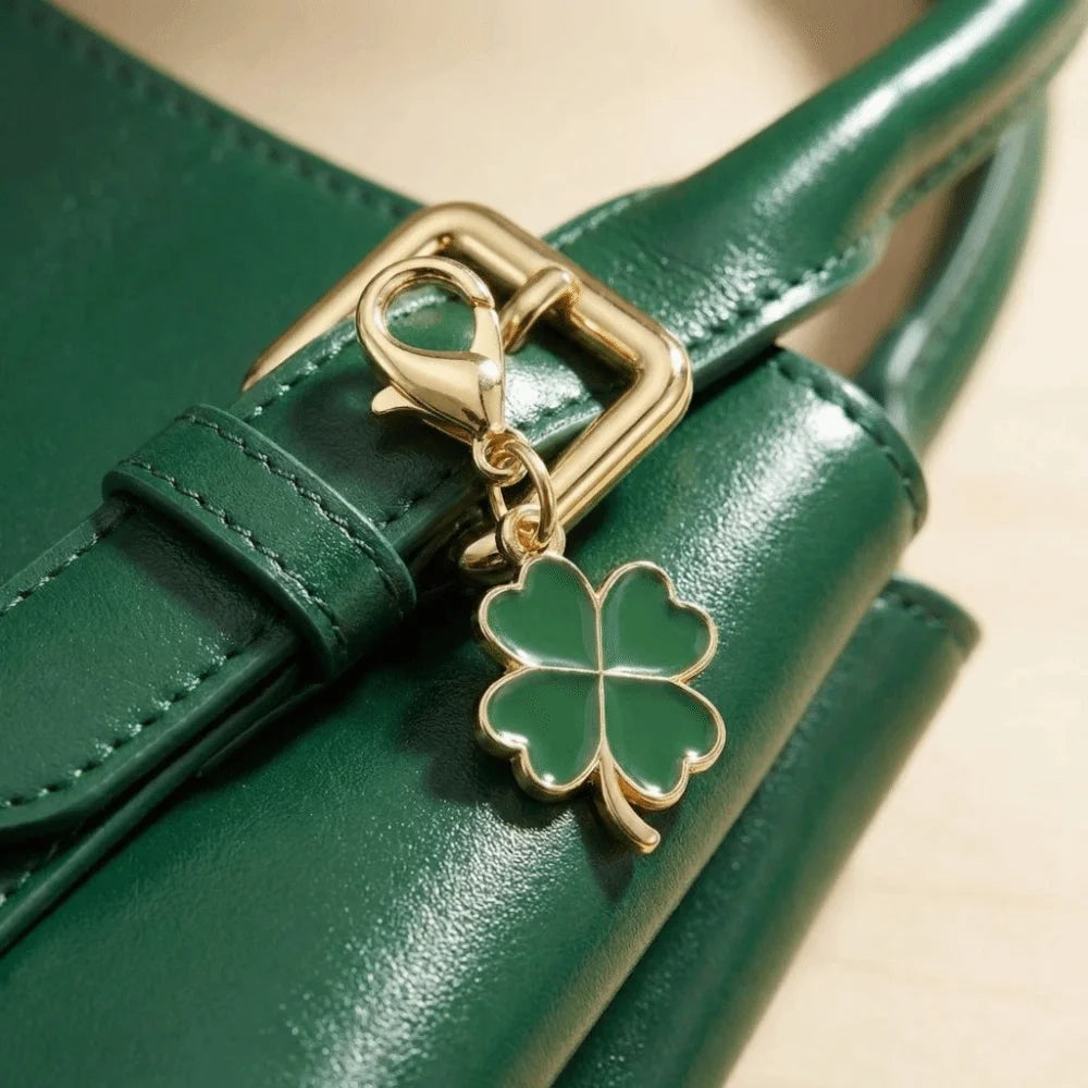 A gold-toned four leaf clover keychain attached to a dark green leather strap.