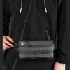 A person wearing a black hoodie is holding a gray multifunctional chest bag.
