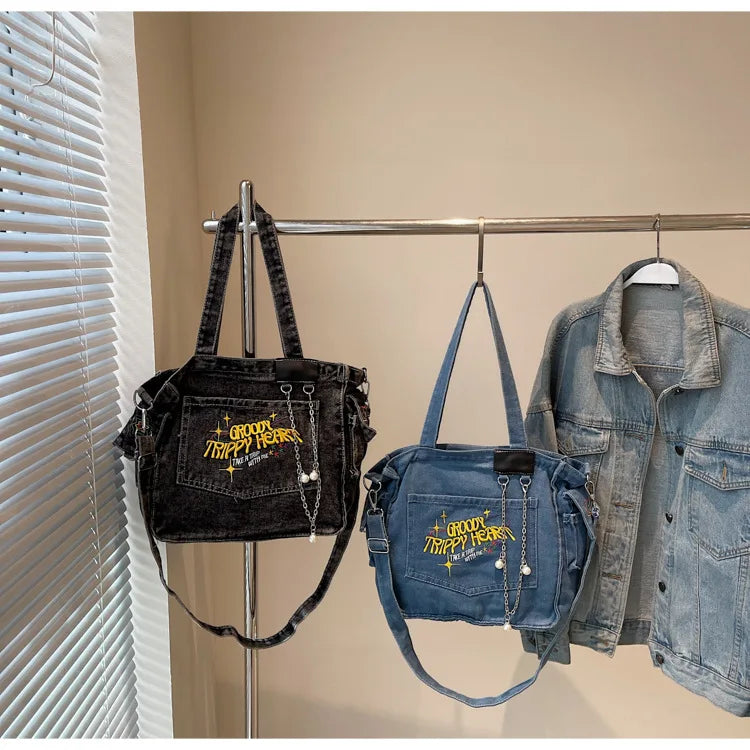 A dark denim crossbody bag is displayed hanging on a rack next to a denim shirt.