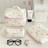 A white quilted makeup bag with pink floral embroidery, a pair of black glasses, and a small white teddy bear.