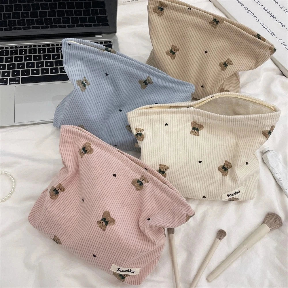 A beige corduroy clutch bag with a textured surface and small brown animal print is shown next to a laptop and makeup brushes