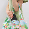 A person holds a large-capacity foldable reusable shopping bag with a tropical floral print.