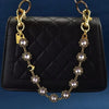 Gold chain necklace with crystal petal charms displayed on a black quilted leather purse.
