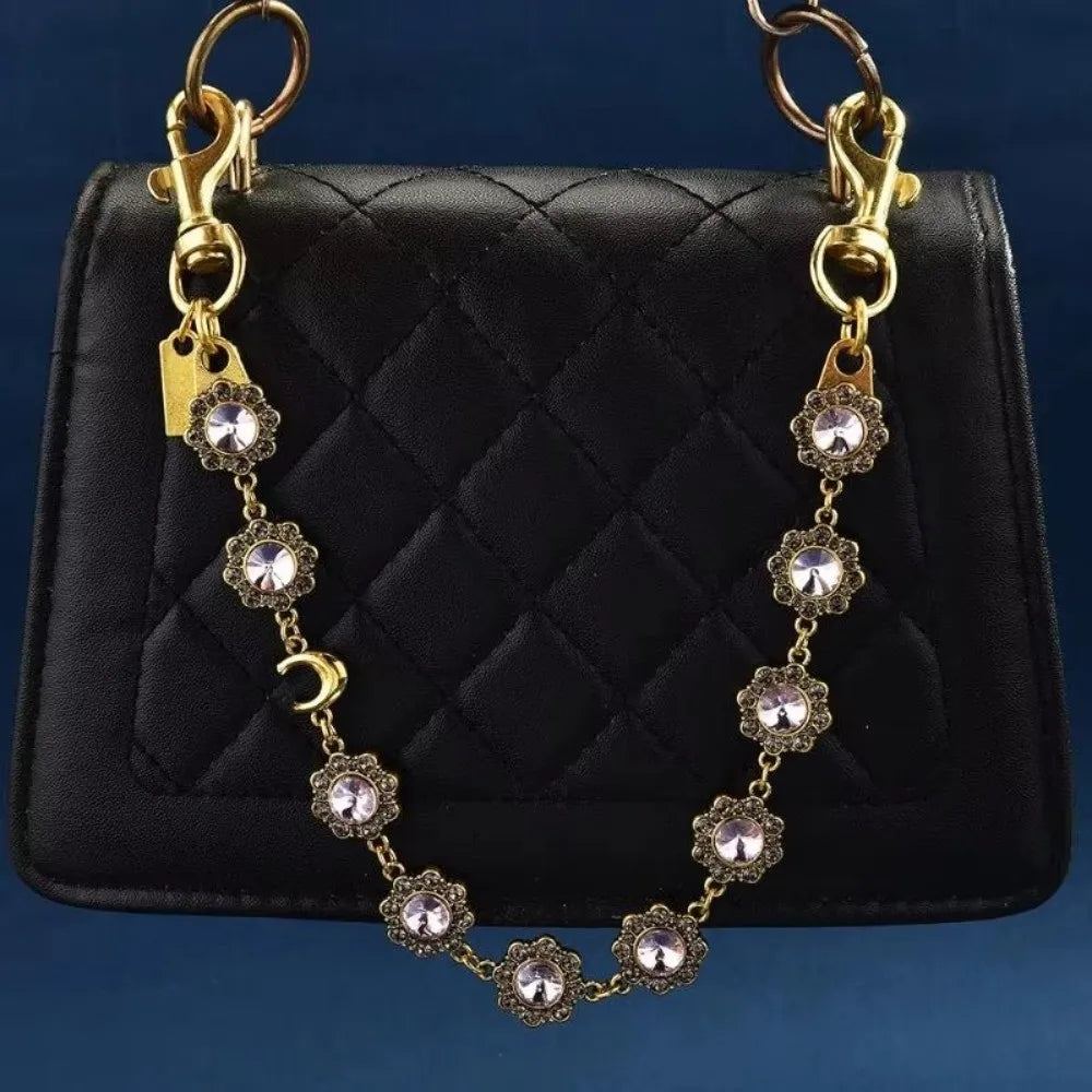 Gold chain necklace with crystal petal charms displayed on a black quilted leather purse.