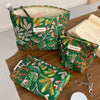 A green fabric cosmetic pouch with an orange floral pattern is shown on a wooden table.