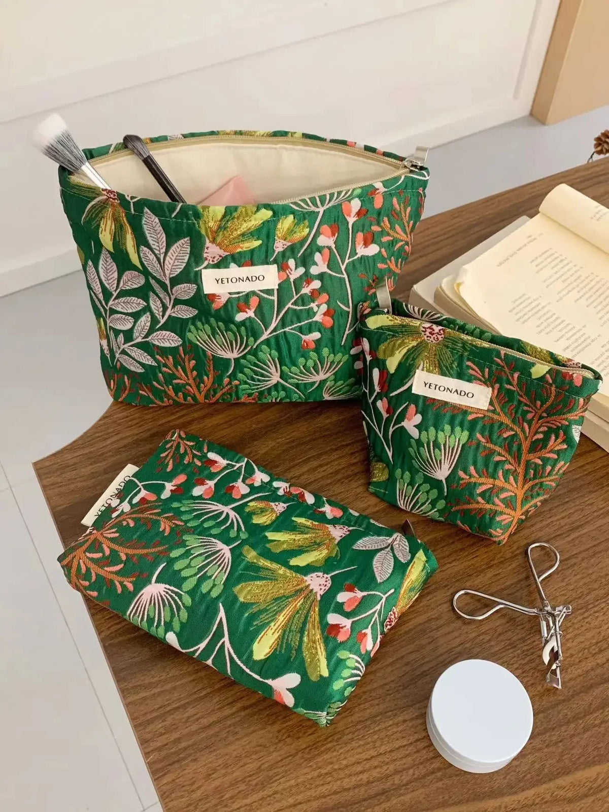 A green fabric cosmetic pouch with an orange floral pattern is shown on a wooden table.