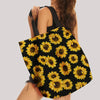 A black canvas tote bag featuring a vibrant yellow sunflower print with reinforced handles.