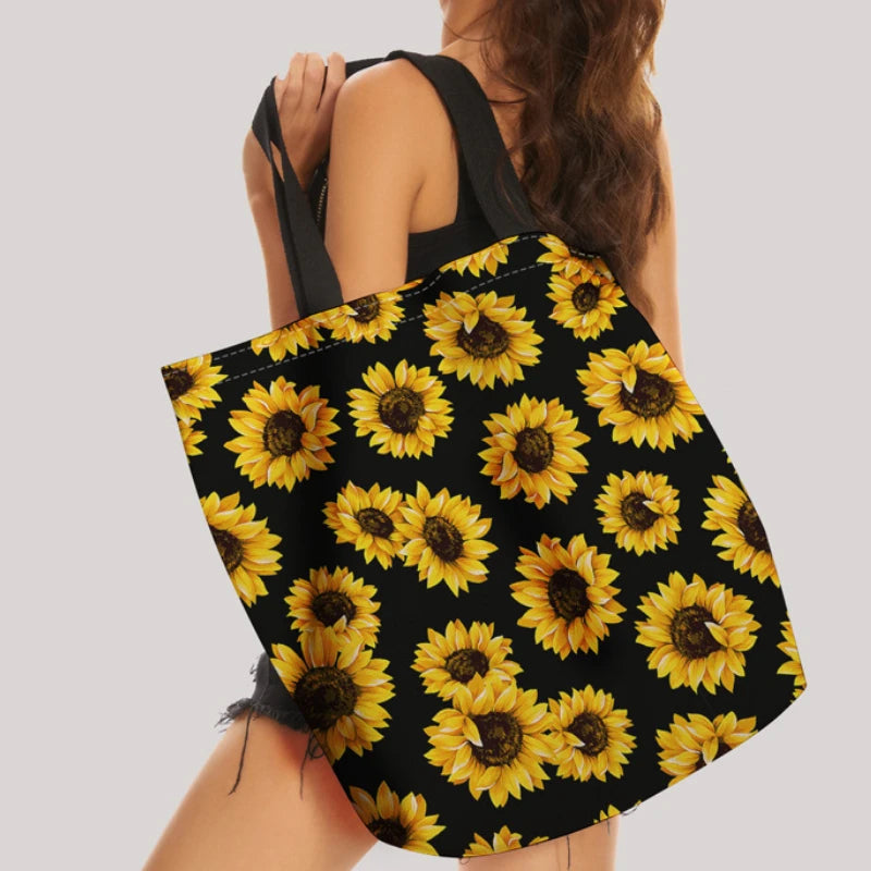 A black canvas tote bag featuring a vibrant yellow sunflower print with reinforced handles.