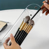 A hand is inserting makeup brushes into a transparent portable organizer pouch.