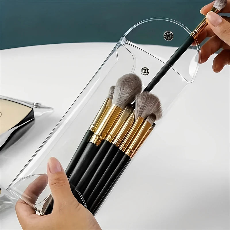 A hand is inserting makeup brushes into a transparent portable organizer pouch.