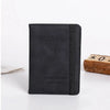 A black passport wallet made of PU leather with a textured finish and stitching, placed next to a wooden block.