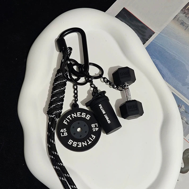 A black D-shape nylon fitness keychain with a fitness disc and attached weights is displayed on a white surface.
