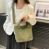 A woman holds a light green canvas crossbody bag with an adjustable strap and multiple pockets.