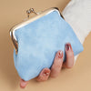 A light blue suede coin purse with a gold buckle is held by a hand against a beige background.