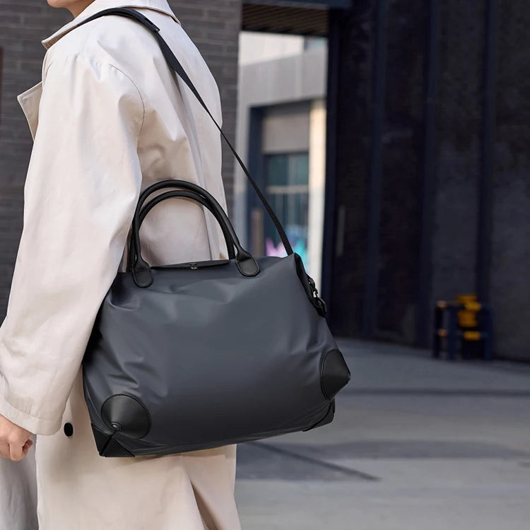 A person is carrying a dark gray durable nylon travel duffle bag over their shoulder.