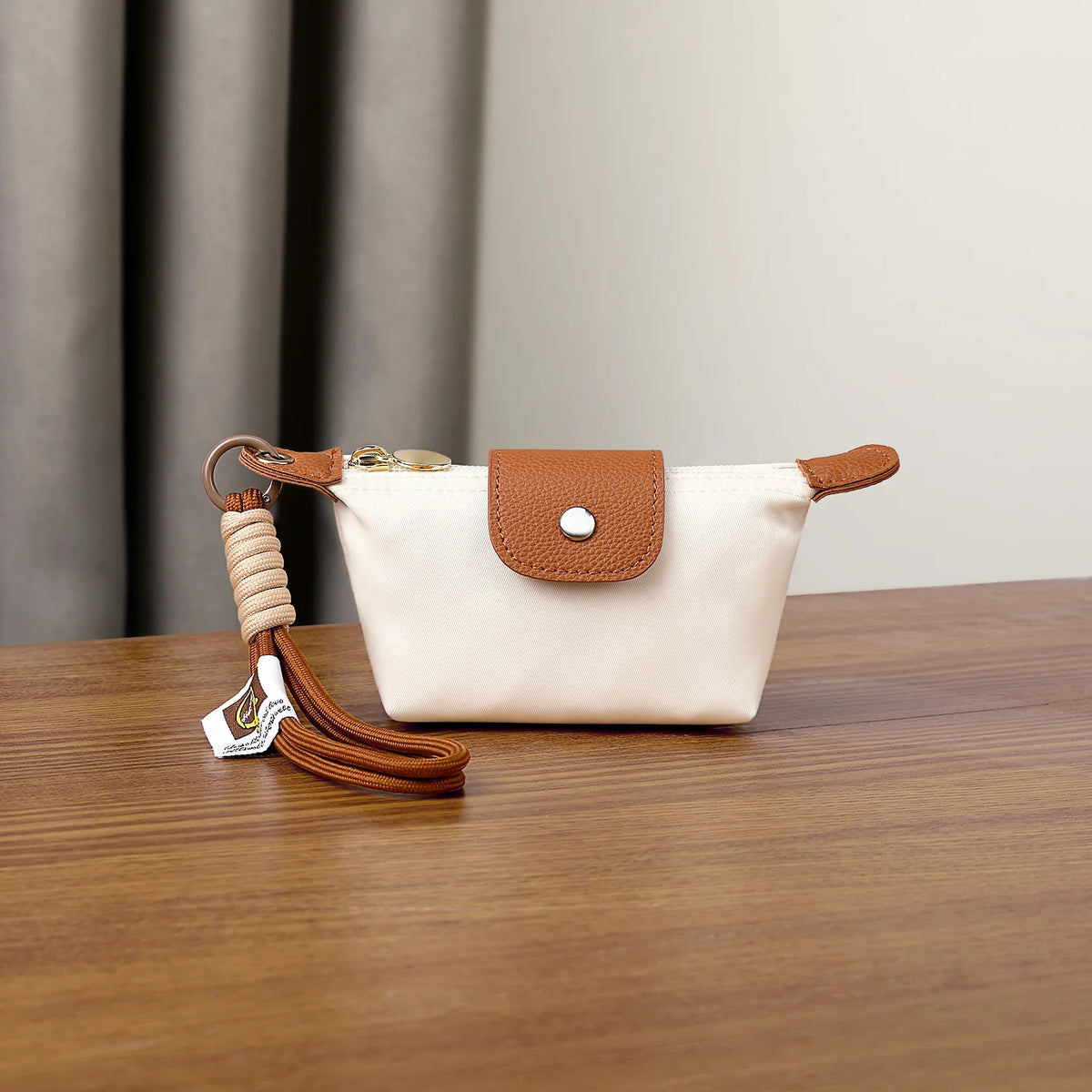 Beige Leder-Geldbörse mit braunem Riemen und Nubukverschluss auf Holzoberfläche.