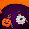 An orange pumpkin shaped mini PU leather keychain accessory with a black bat silhouette in a dark purple Halloween themed set