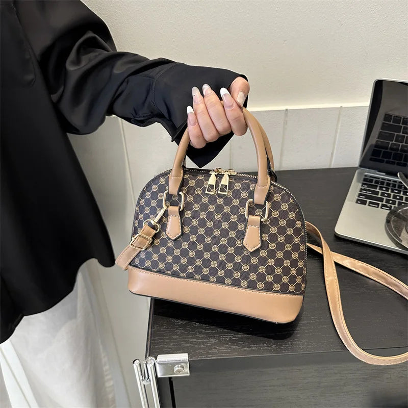 A woman's hand holds a tan fashion shell shoulder crossbody bag with a checkered pattern against a dark surface.
